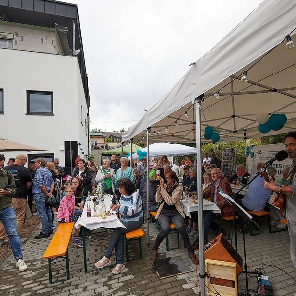 Stephan Brings begleitet sich beim Singen selbst mit der Gitarre. Die Gäste der Einweihungsfeier hören zu, im Hintergrund das neu gebaute Haus