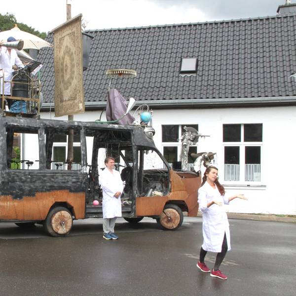 Die futuristische Klima-Galeere des Künstlers Peter Ratz steht auf einem Platz. Zwei Künstler in weißen Kitteln stehen davor, einer darauf.
