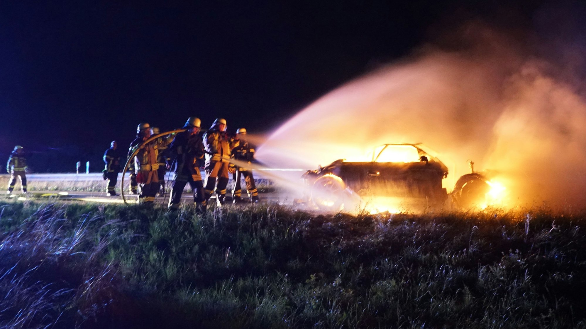 Mit mehreren Strahlrohren löschen Feuerwehrleute den lichterloh brennenden Wagen.