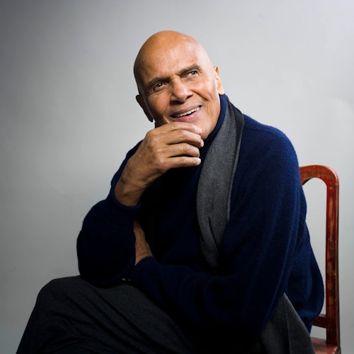 Harry Belafonte sitzt auf einem Stuhl und lächelt.