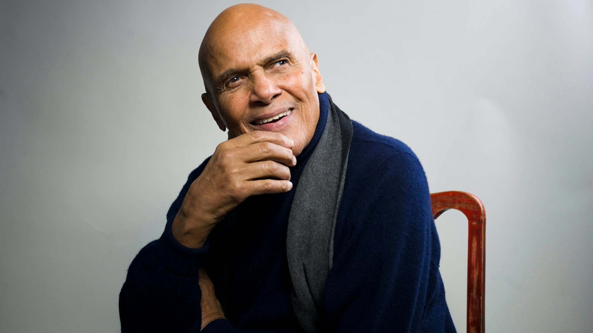 Harry Belafonte sitzt auf einem Stuhl und lächelt.