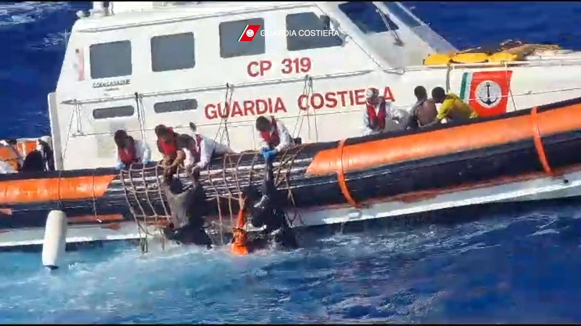 Retter versuchen den Migranten beim Einsteigen in ein Rettungsboot zu helfen.