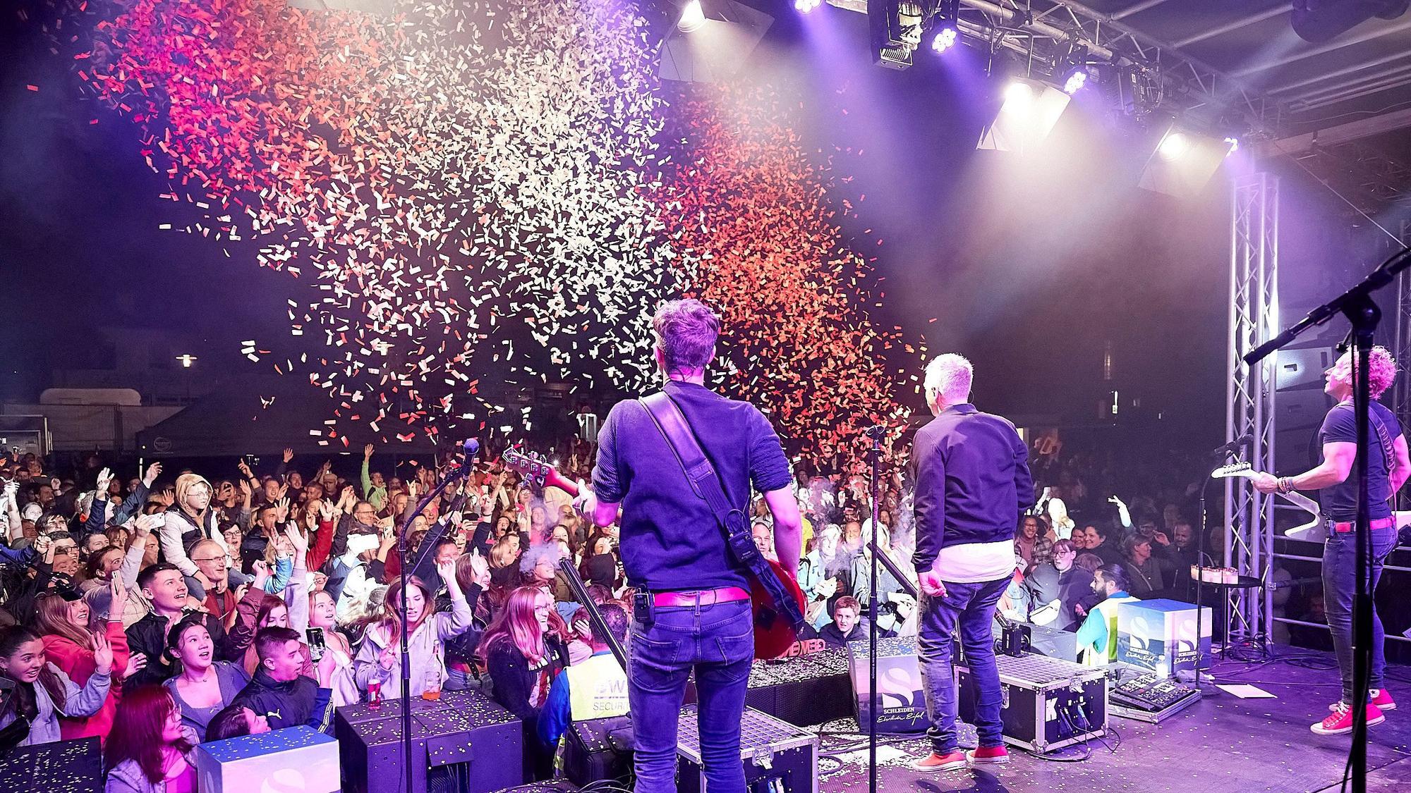 Das Bild zeigt von hinten Musiker der Kölner Band Kasalla. Aus einer Kanone wird rot-weißes Konfetti auf die Zuschauer geschossen.