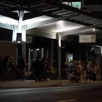 Menschen sitzen vor einem Bahnhof.