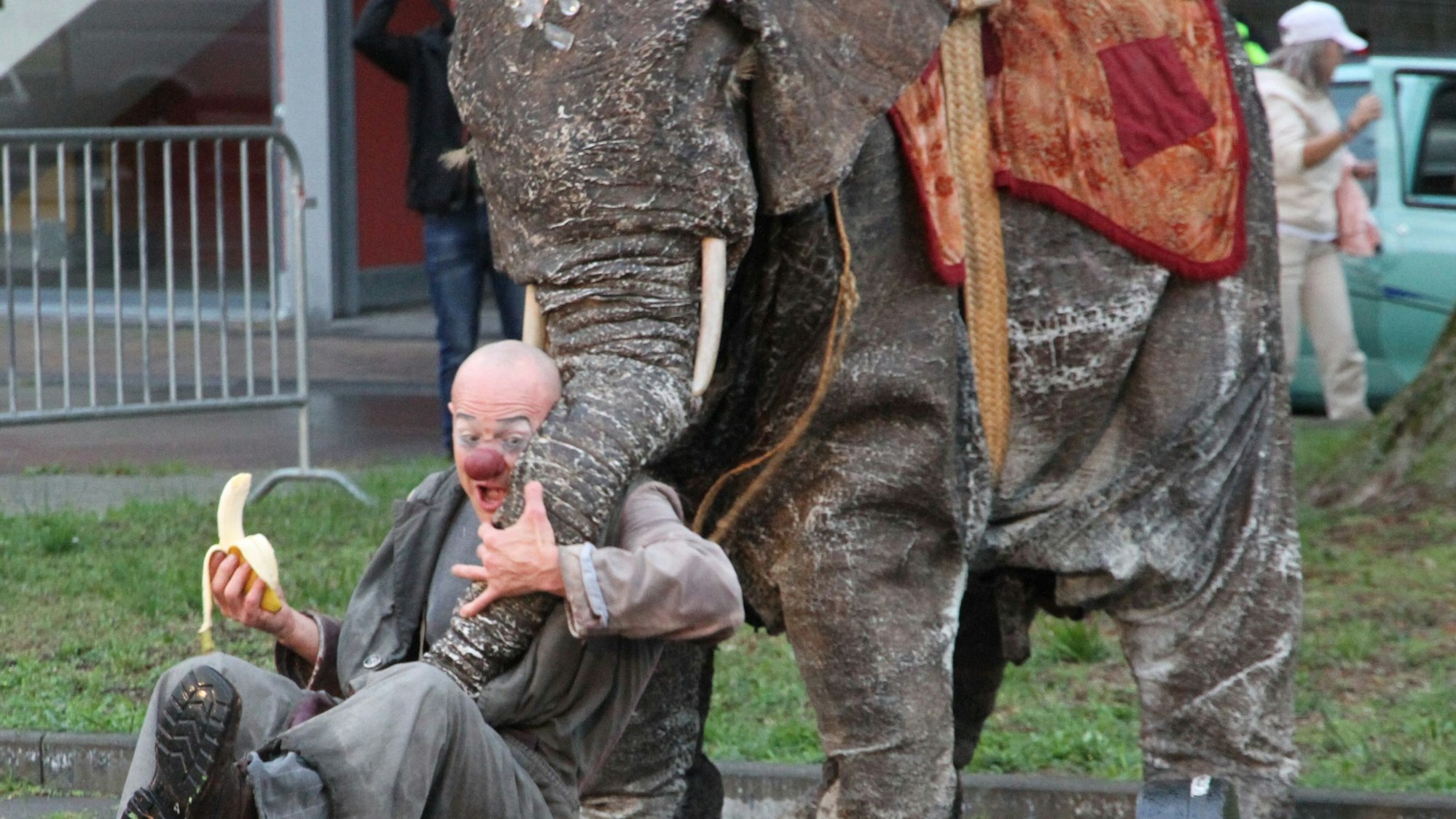 Ein von Schauspielern gespielter Elefant will einem Clown eine Banane abnehmen