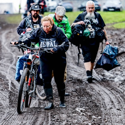 06.08.2023, Schleswig-Holstein, Wacken: Festivalbesucher verlassen das verschlammte Campinggelände des Wacken Open Air mit ihren Fahrrädern. Foto: Axel Heimken/dpa +++ dpa-Bildfunk +++