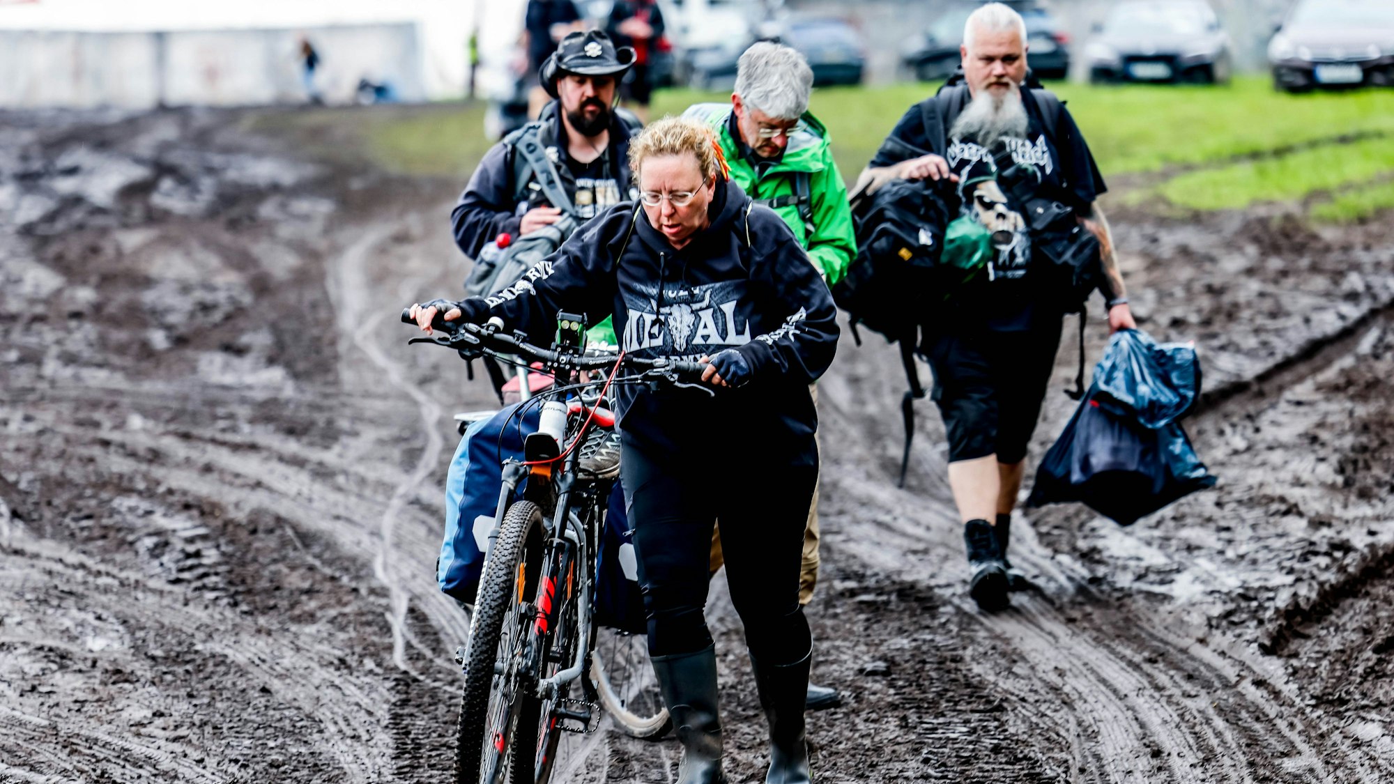 06.08.2023, Schleswig-Holstein, Wacken: Festivalbesucher verlassen das verschlammte Campinggelände des Wacken Open Air mit ihren Fahrrädern. Foto: Axel Heimken/dpa +++ dpa-Bildfunk +++
