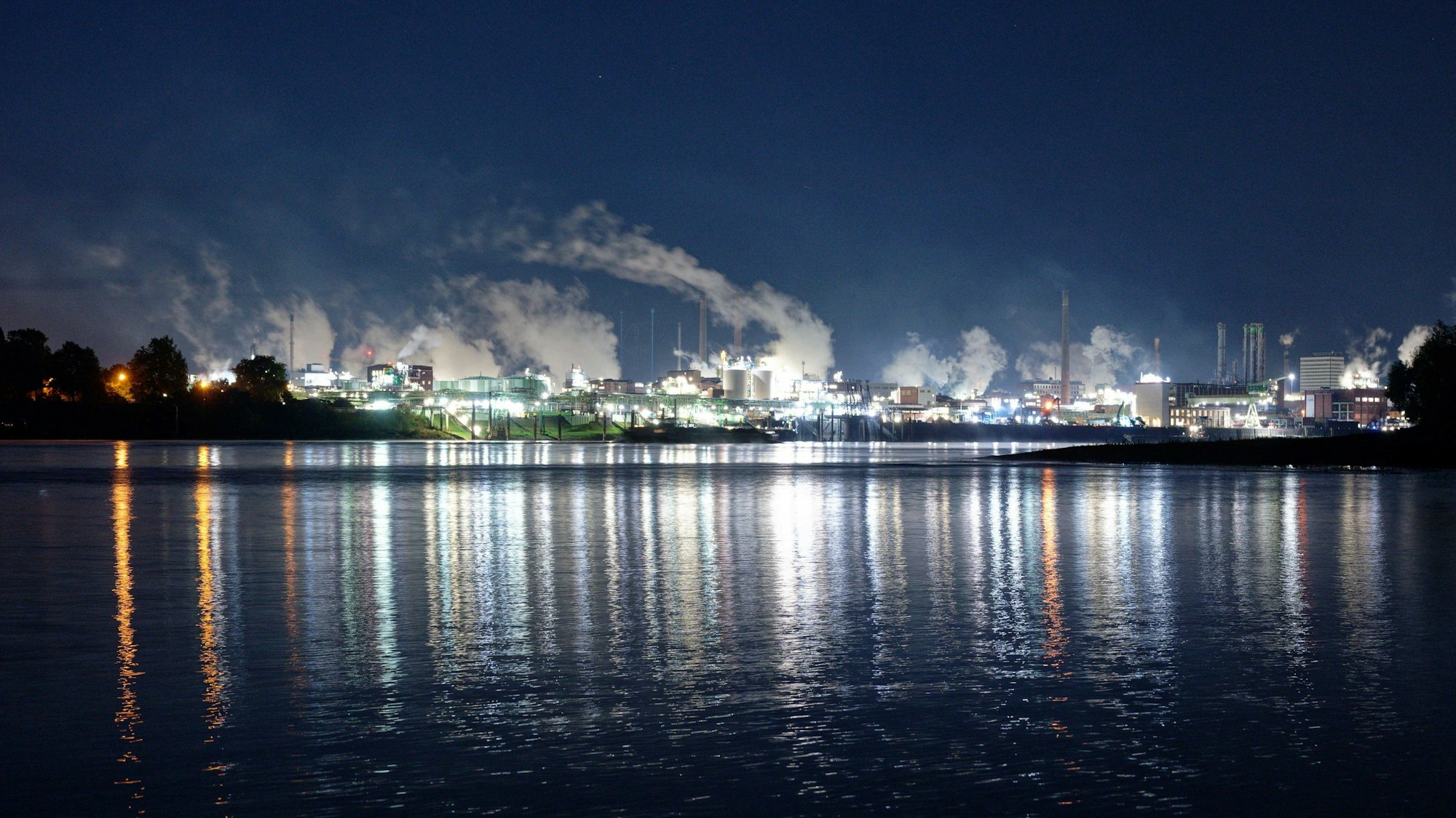 29.09.2022, Nordrhein-Westfalen, Leverkusen: Die Lichter des Chemparks in Leverkusen spiegeln sich im Wasser des Rheins.