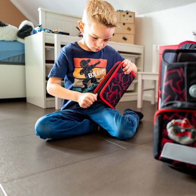 Grundschüler Lion Preiser sitzt auf dem Boden und öffnet sein neues Mäppchen.