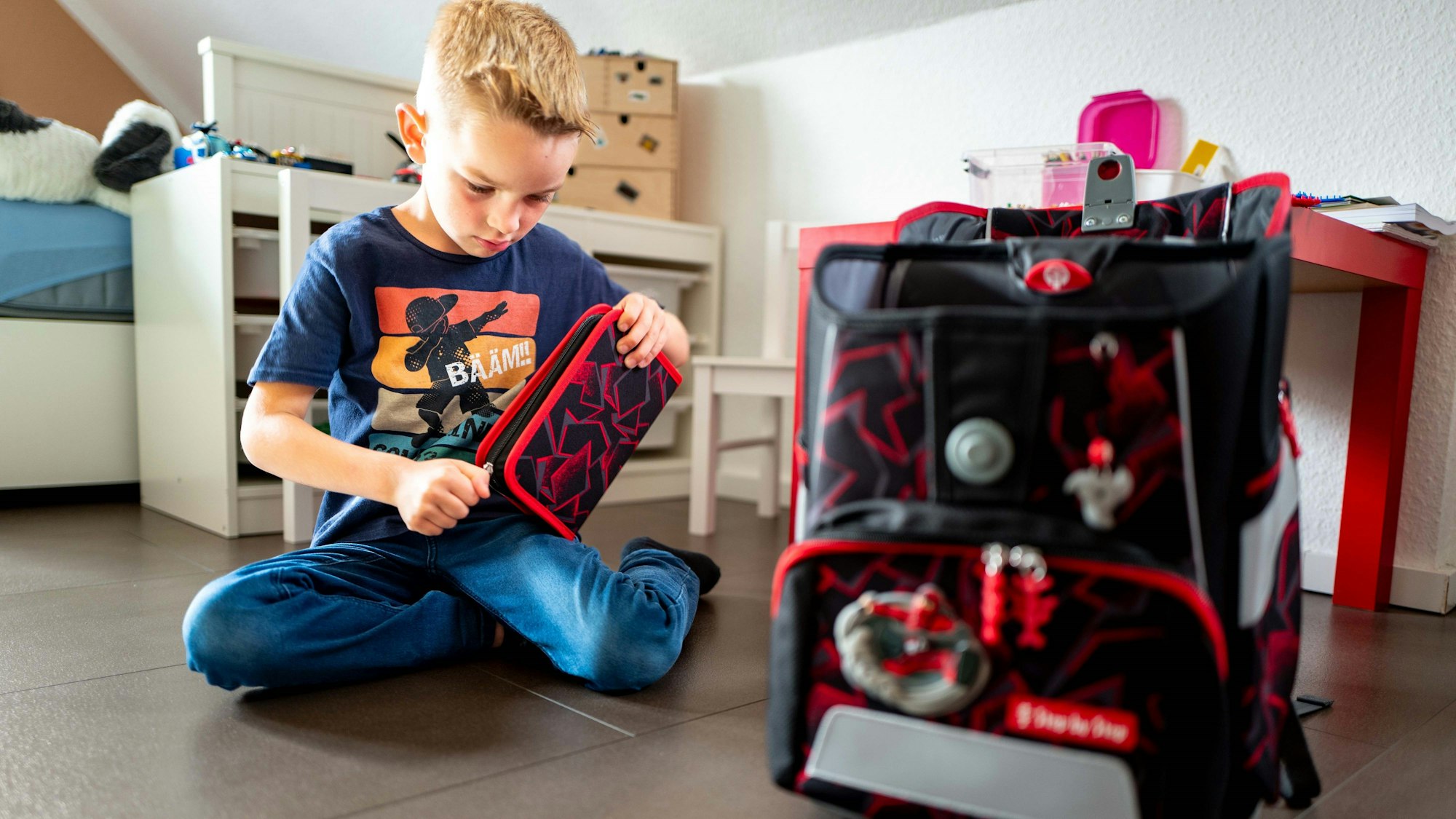 Grundschüler Lion Preiser sitzt auf dem Boden und öffnet sein neues Mäppchen.