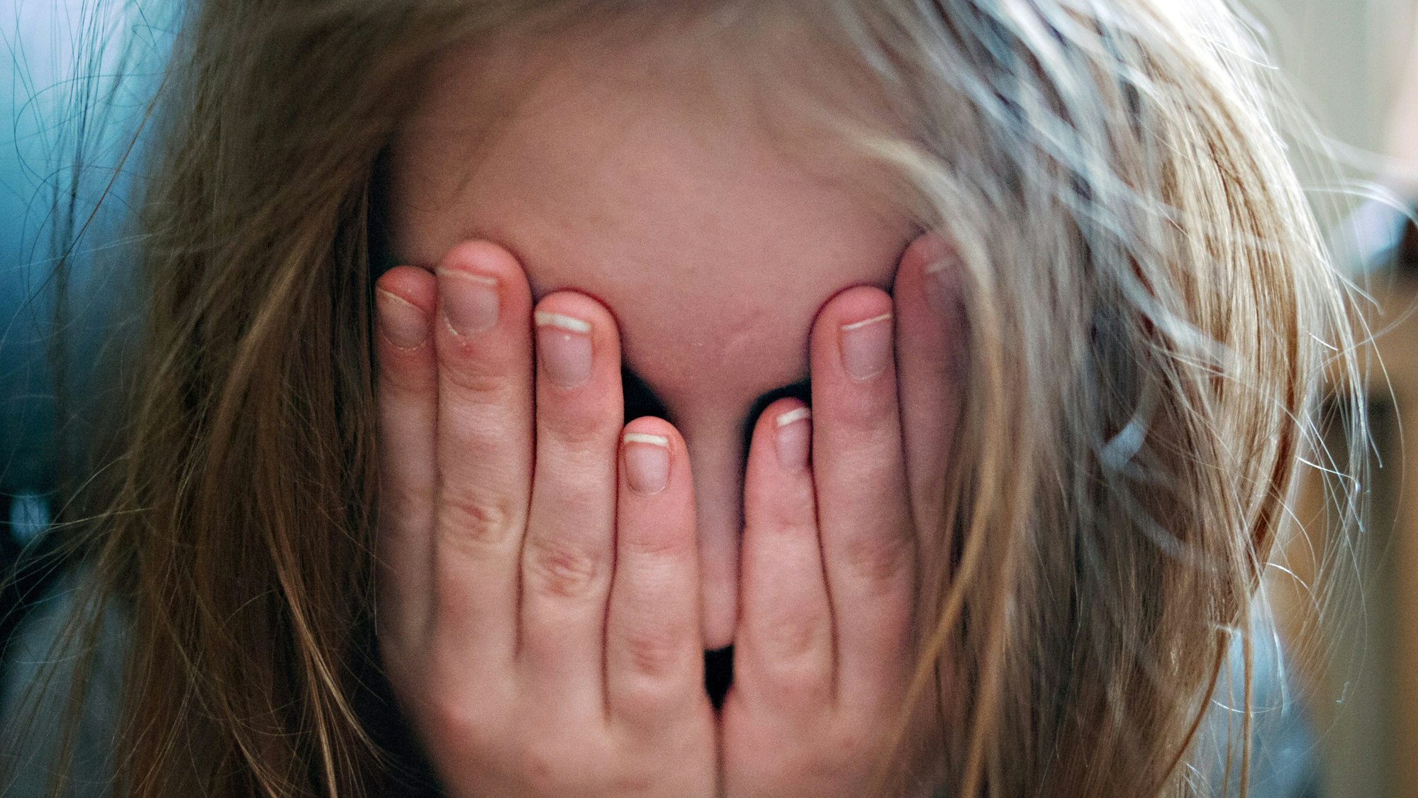 Ein junges Mädchen hält sich die Hände vor ihr Gesicht.