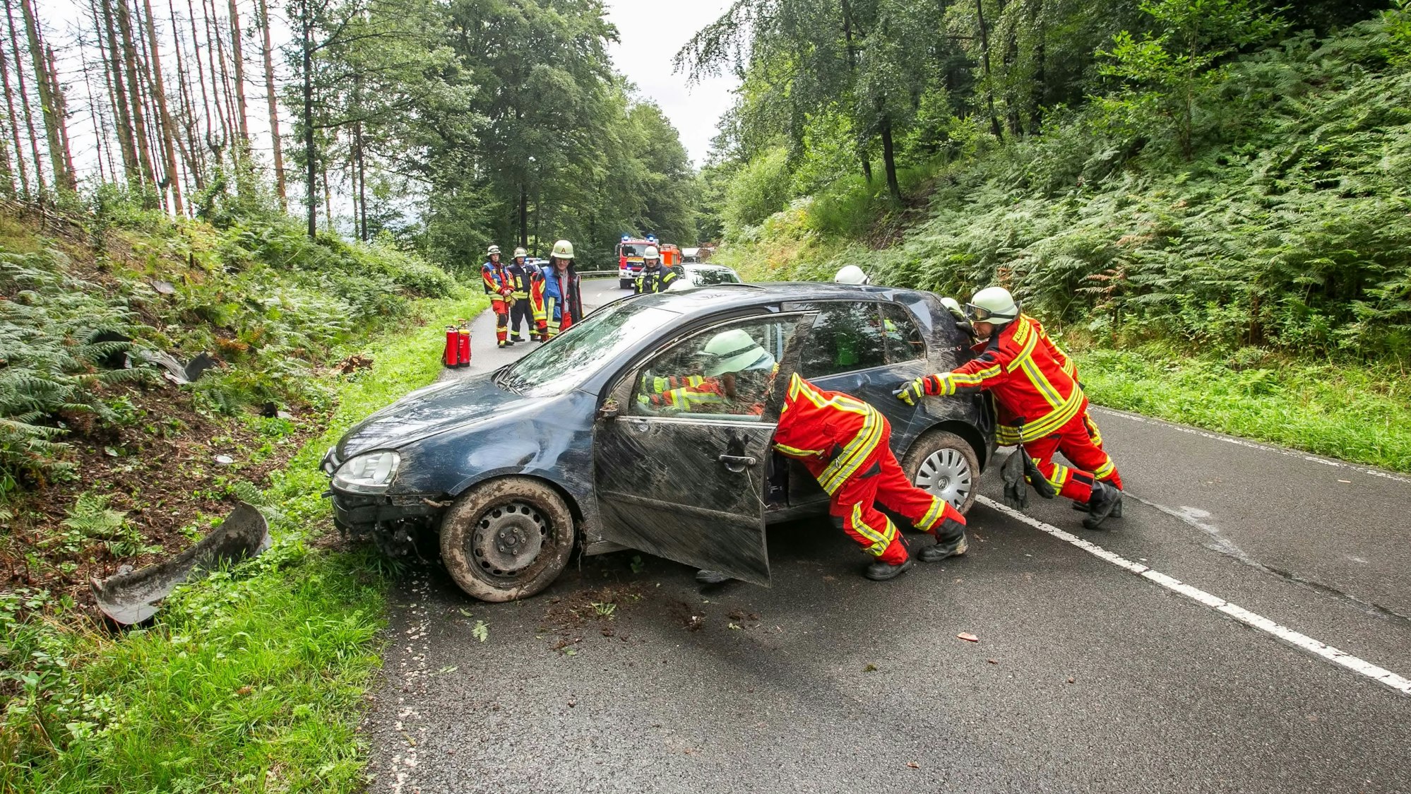 Mehrere Feuerwehrleute schieben ein Unfallauto von der Straße.