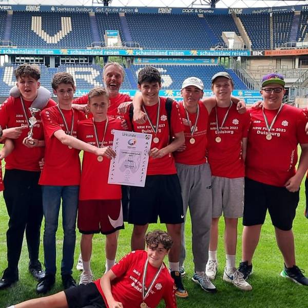 Eine Reihe von Schülerinnen und Schülern in Trikots vor der Tribüne eines Stadions.