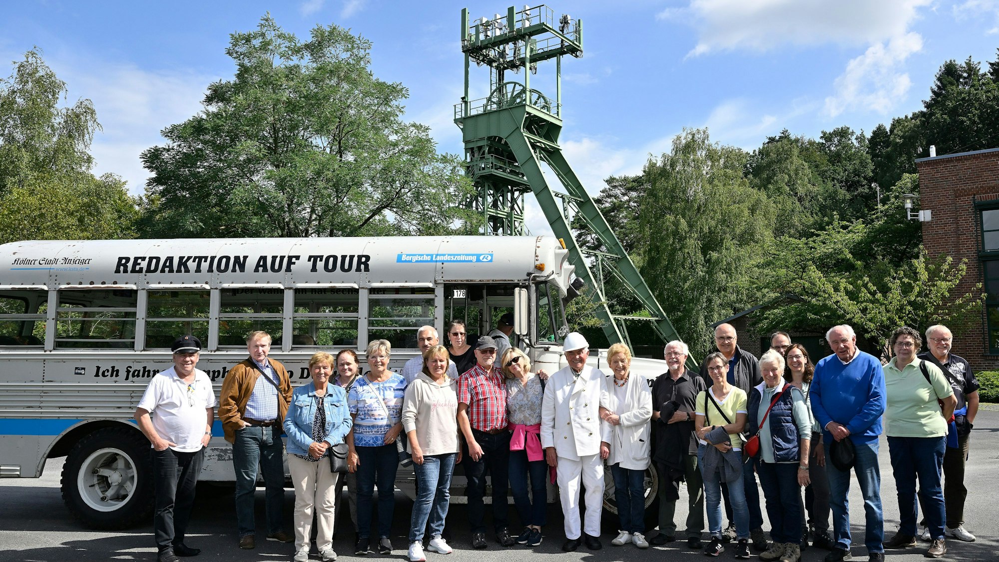 Eine Gruppe steht vor einem historischen amerikanischen Schulbus, der vor dem Förderturm eines ehemaligen BErgwerks parkt.