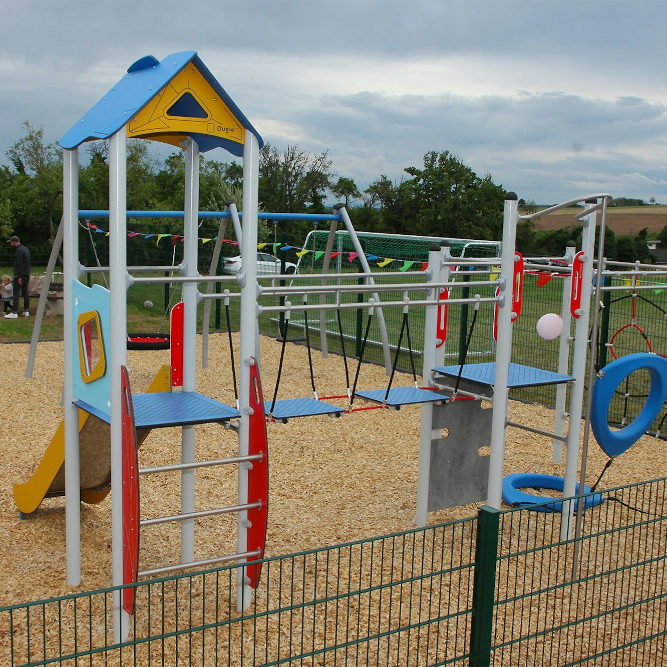Ein Klettergerüst mit Rutsche steht in einem umzäunten Gelände.