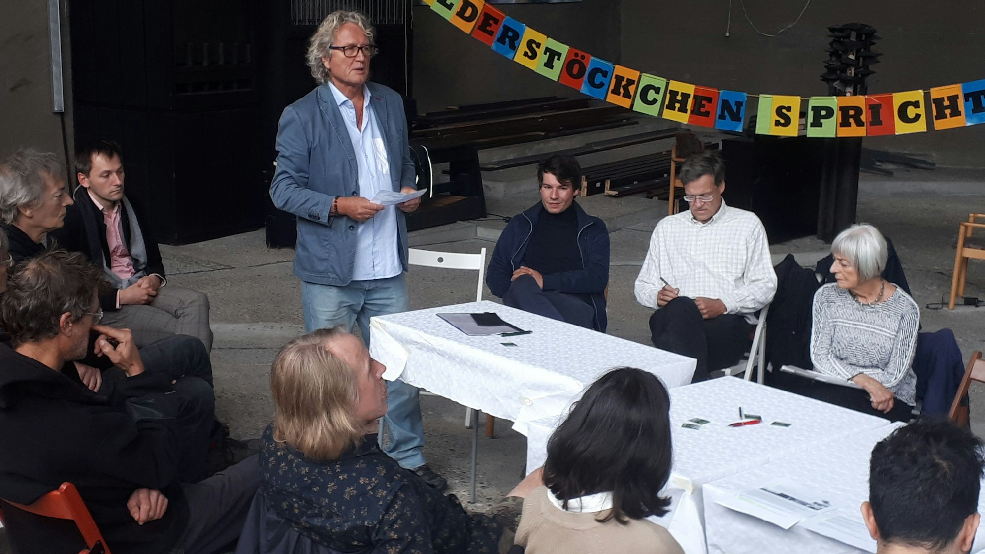 Ein Mann steht vor einem Tisch, an dem Gäste sitzen.