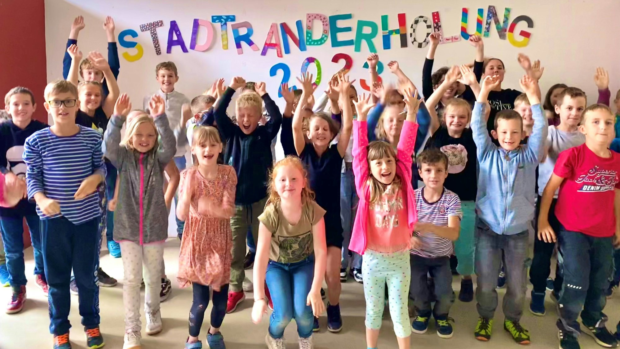 Eine Gruppe von Kindern, die an der Stadtranderholung 2023 teilgenommen haben, reißt die Arme in die Luft.