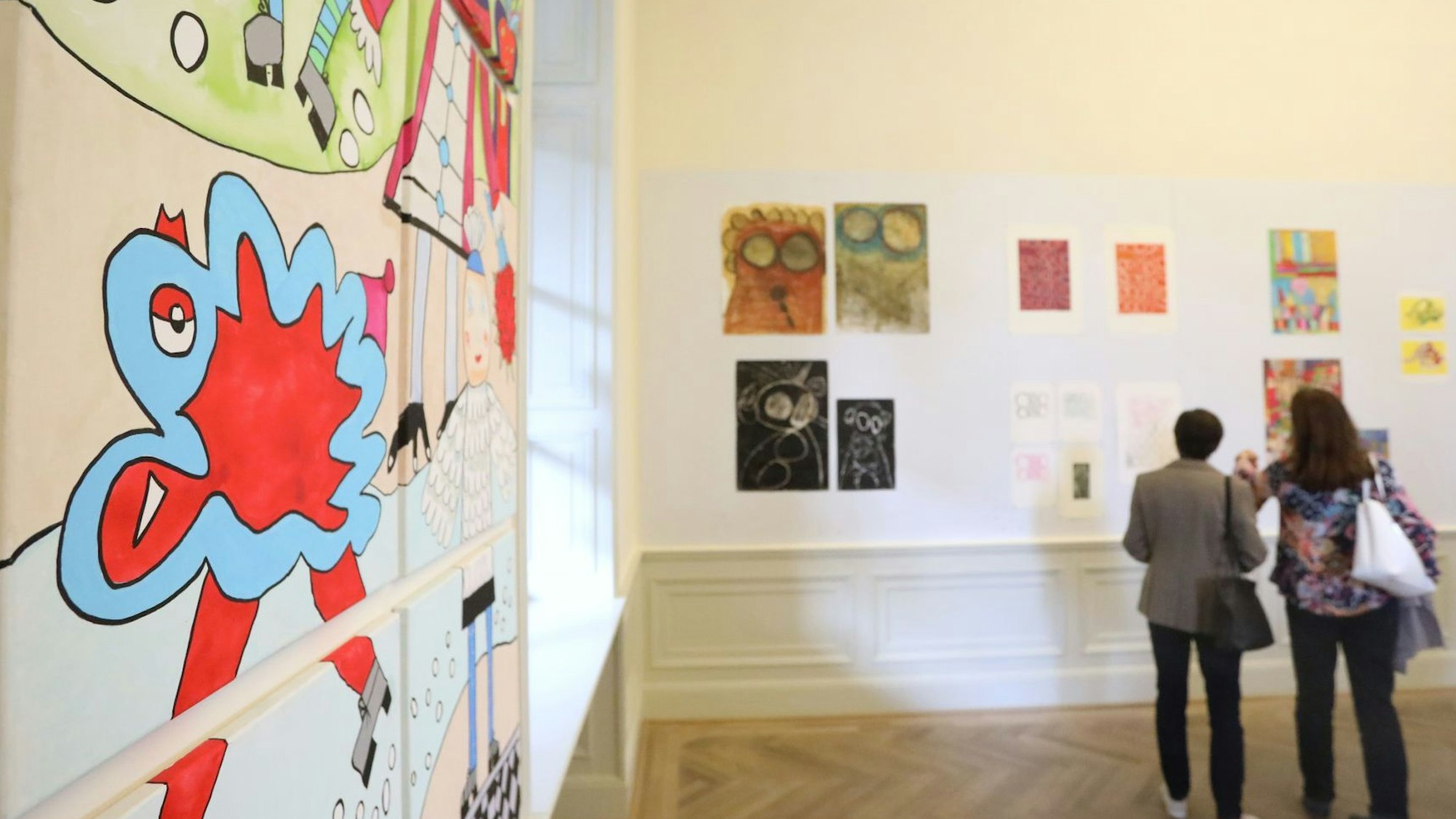 Blick in den Ausstellungsraum. Im Hintergrund betrachten zwei Personen die Werke.