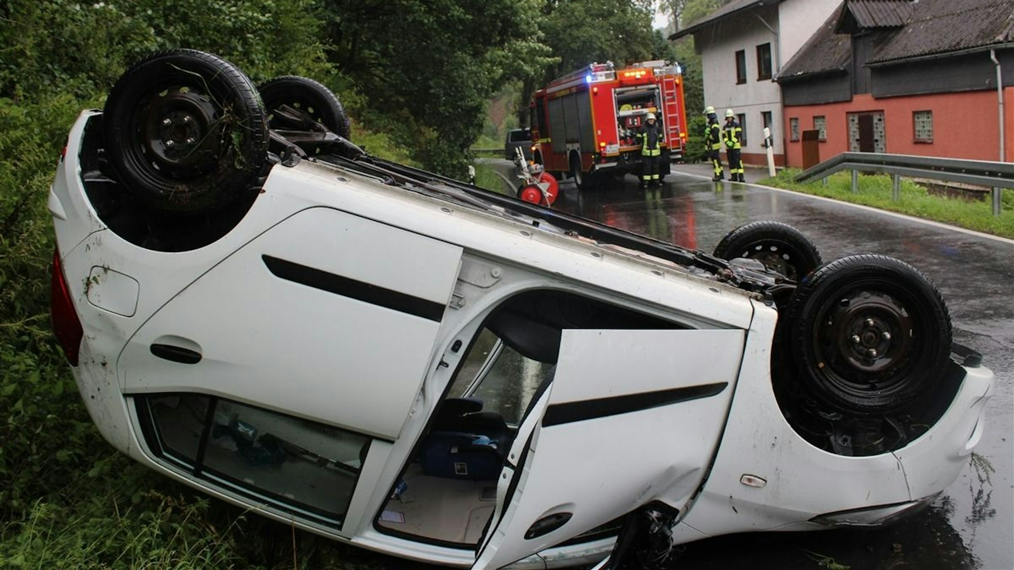 Ein weißes Auto liegt auf dem Dach, eine Tür ist offen.