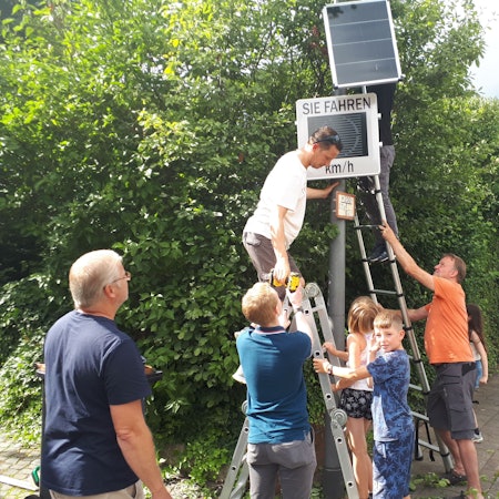 Freiwillige Helfer montierten mit vereinten Kräften die neue Tempo-Infotafel an der Longericher Straße.