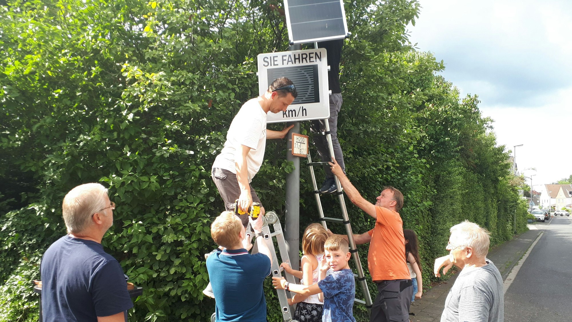 Freiwillige Helfer montierten mit vereinten Kräften die neue Tempo-Infotafel an der Longericher Straße.