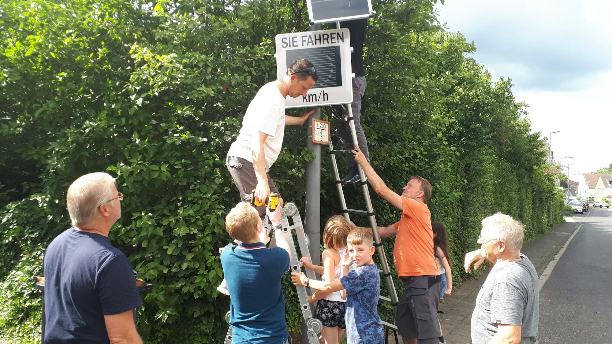 Freiwillige Helfer montierten mit vereinten Kräften die neue Tempo-Infotafel an der Longericher Straße.