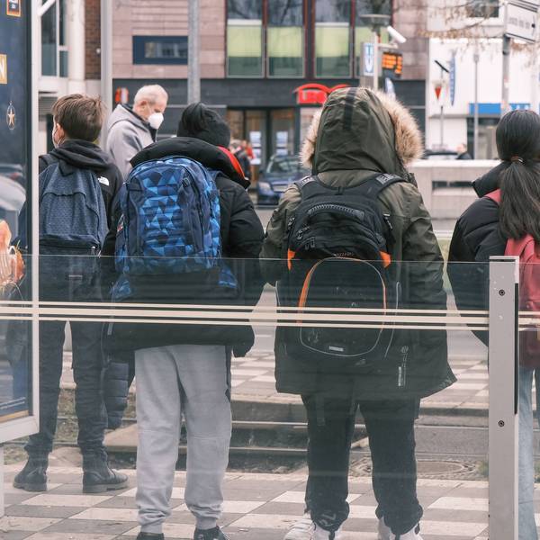 Kinder mit Schulrucksäcken stehen an einer Bahnhaltestelle.