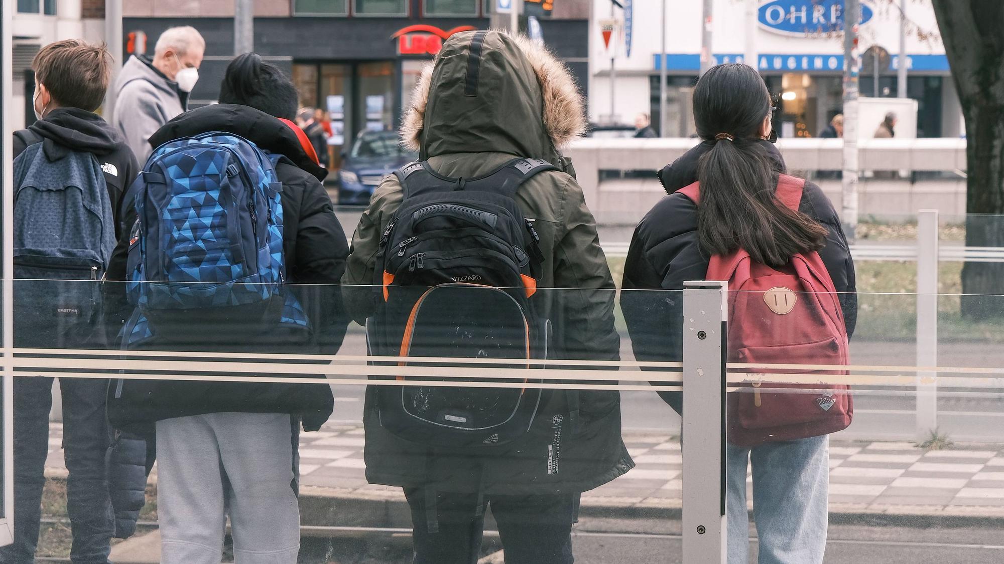 Kinder mit Schulrucksäcken stehen an einer Bahnhaltestelle.