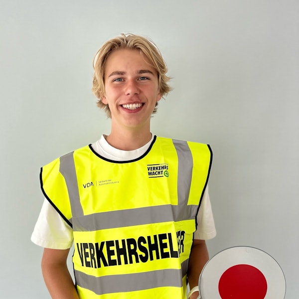 Schülerlotse Paul Grastat trägt ein gelbe Warnweste und lacht in die Kamera.