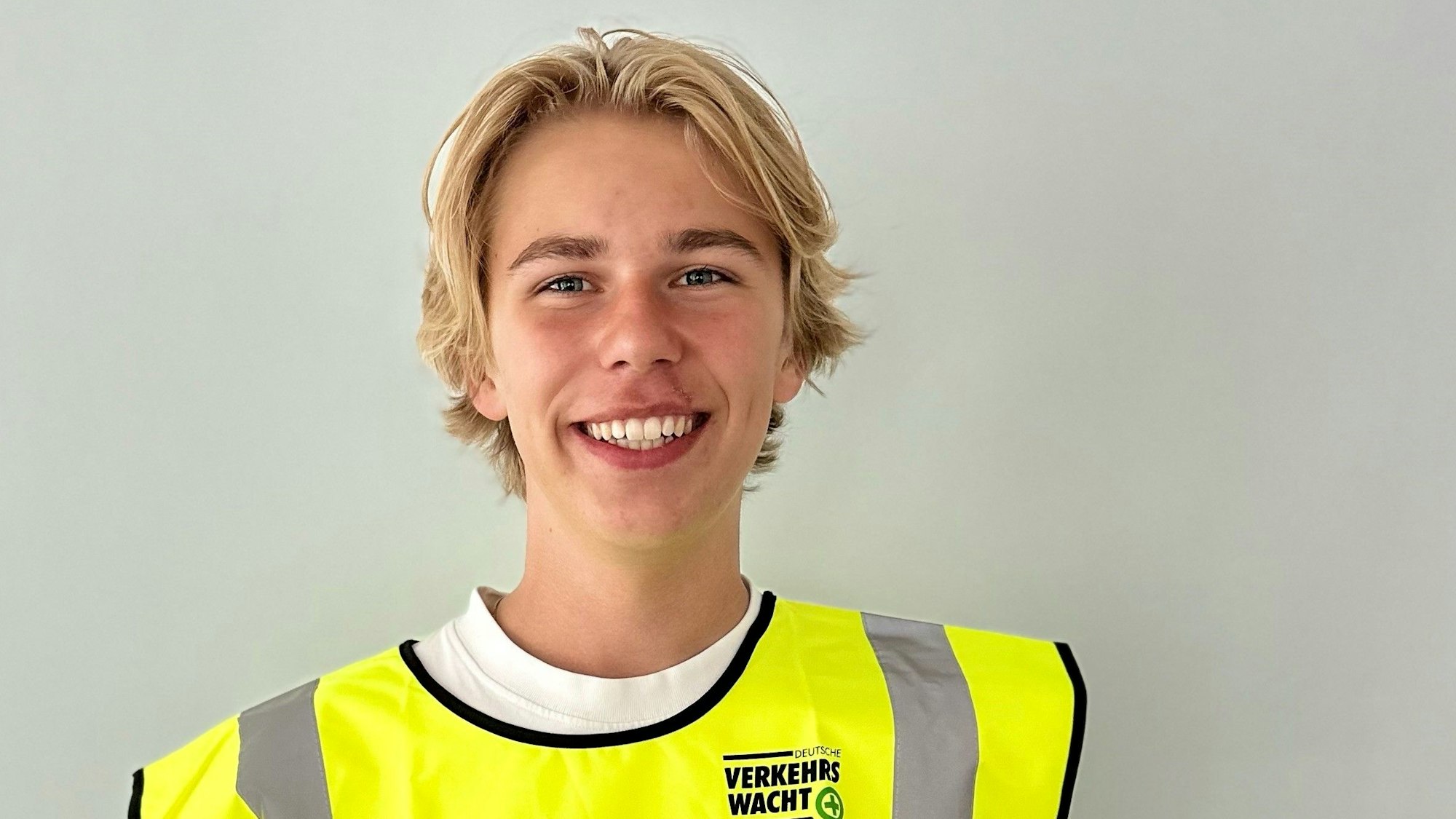 Schülerlotse Paul Grastat trägt ein gelbe Warnweste und lacht in die Kamera.