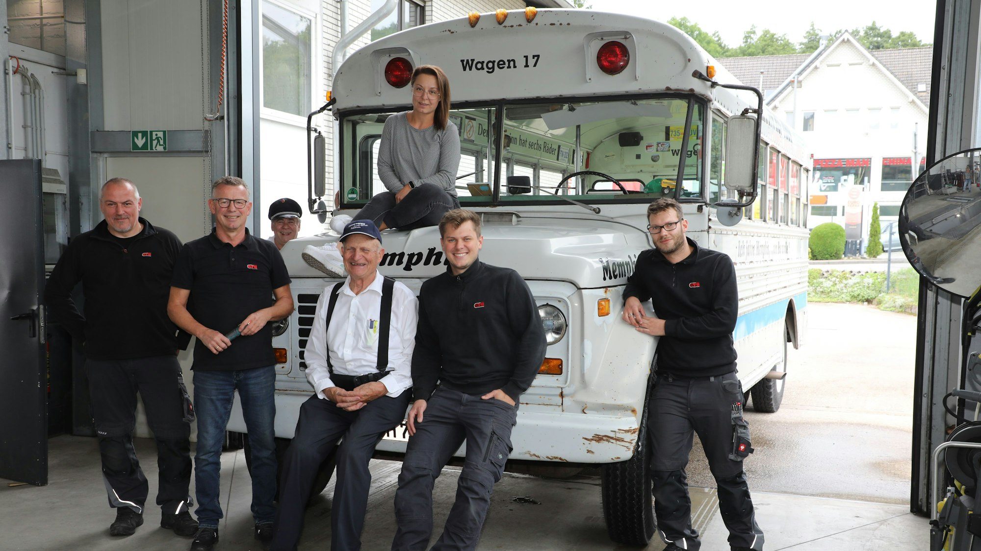 Ein historischer Bus steht an der Einfahrt zu einer Werkstatthalle, davor stehen Menschen.