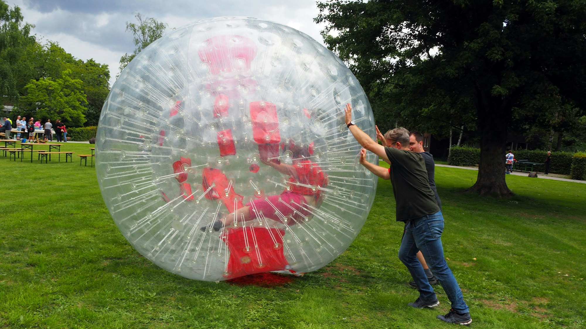 Zwei Männer rollen einen riesigen Plastikball, in dem eine Frau versucht, zu laufen.
