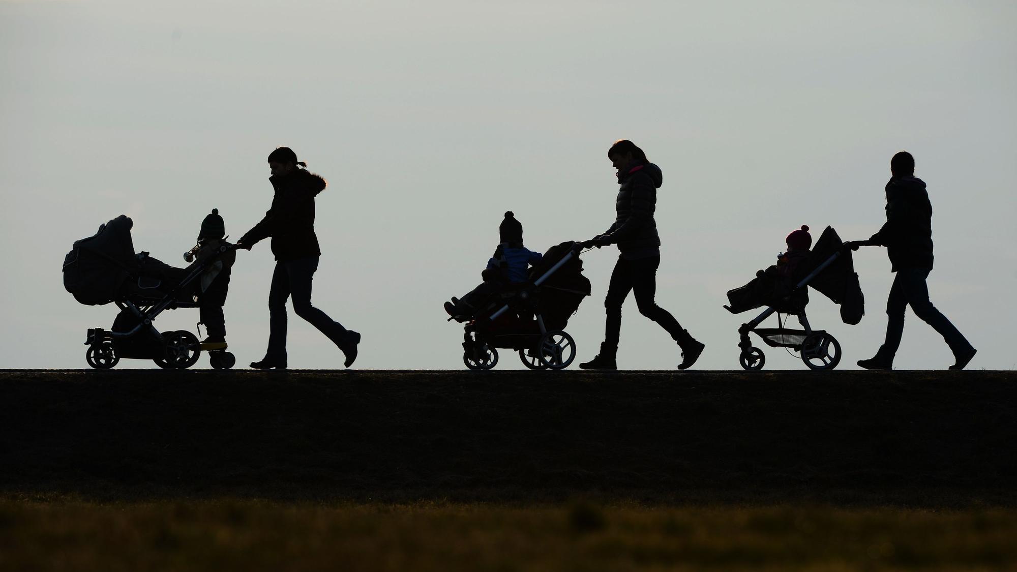 Mütter schieben ihre Kinderwagen eine Straße entlang.