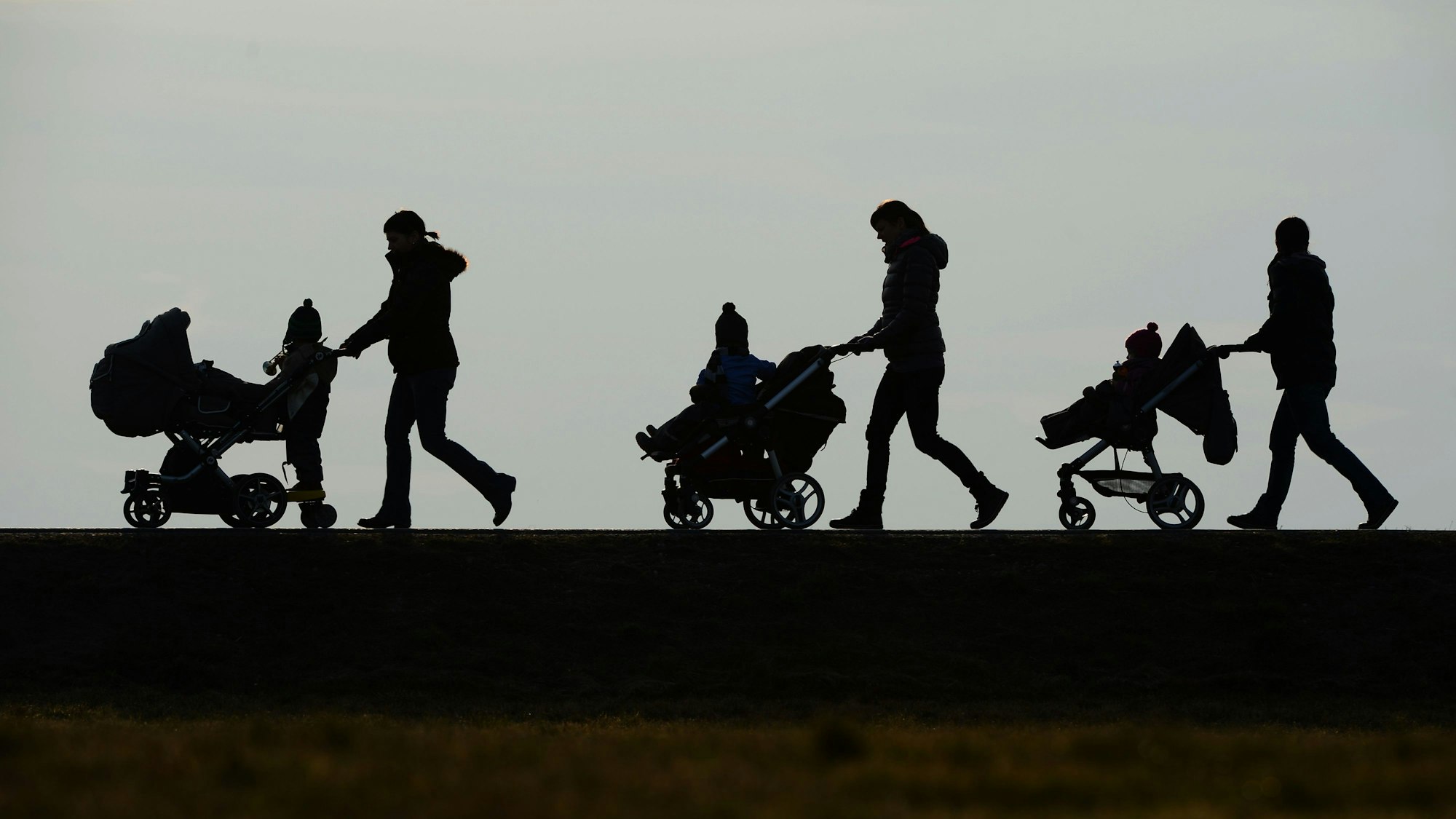 Mütter schieben ihre Kinderwagen eine Straße entlang.