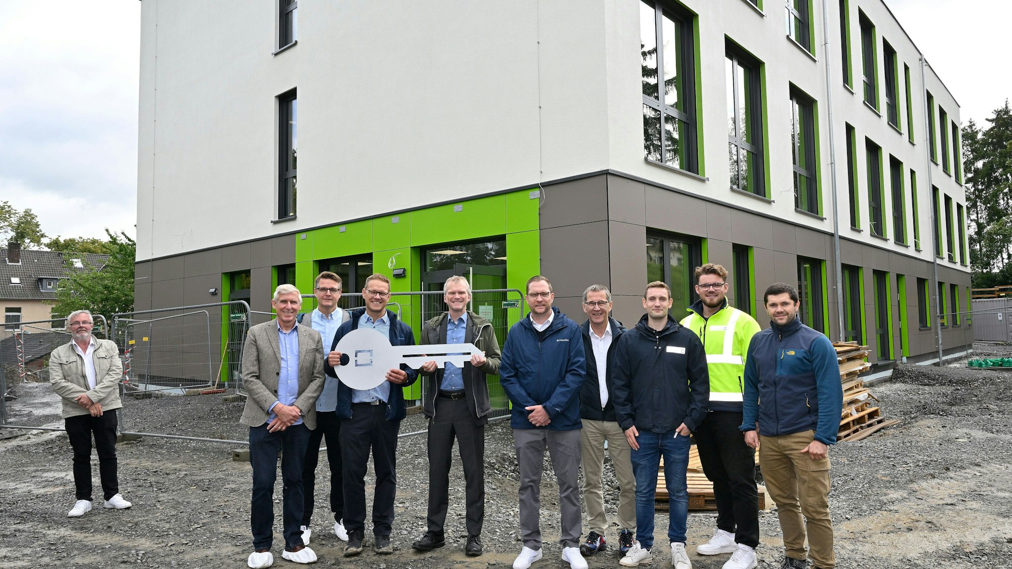 Vor dem Neubau der Modulschule steht der Bürgermeister mit den am Projekt beteiligten Fachleuten. Sie halten einen großen symbolischen Schlüssel in der Hand.