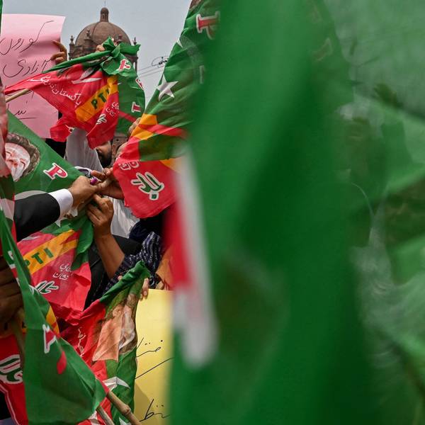 Menschen halten Banner hinter einer unscharfen pakistanischen Flagge hoch. (Symbolbild)