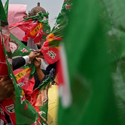 Menschen halten Banner hinter einer unscharfen pakistanischen Flagge hoch. (Symbolbild)