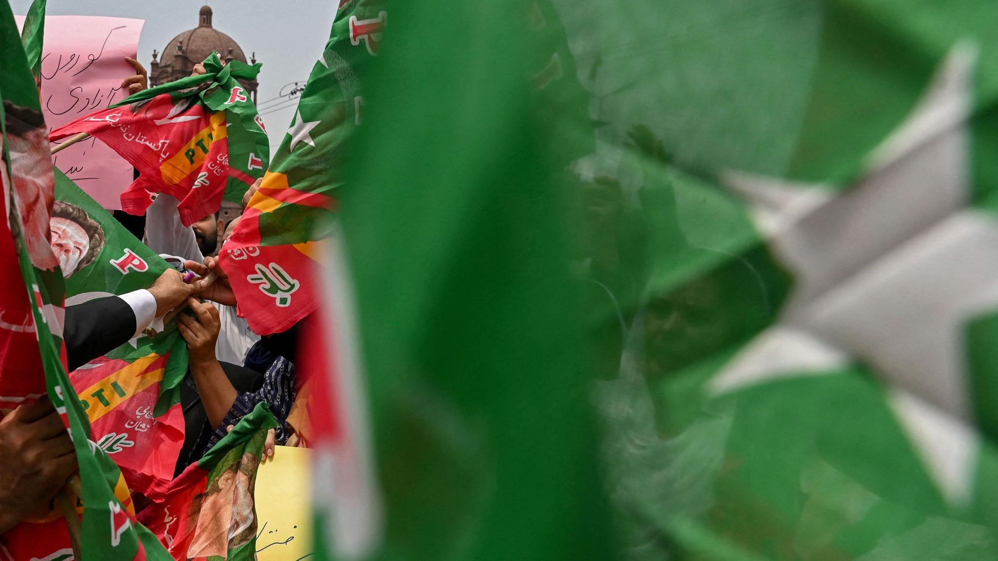 Menschen halten Banner hinter einer unscharfen pakistanischen Flagge hoch. (Symbolbild)