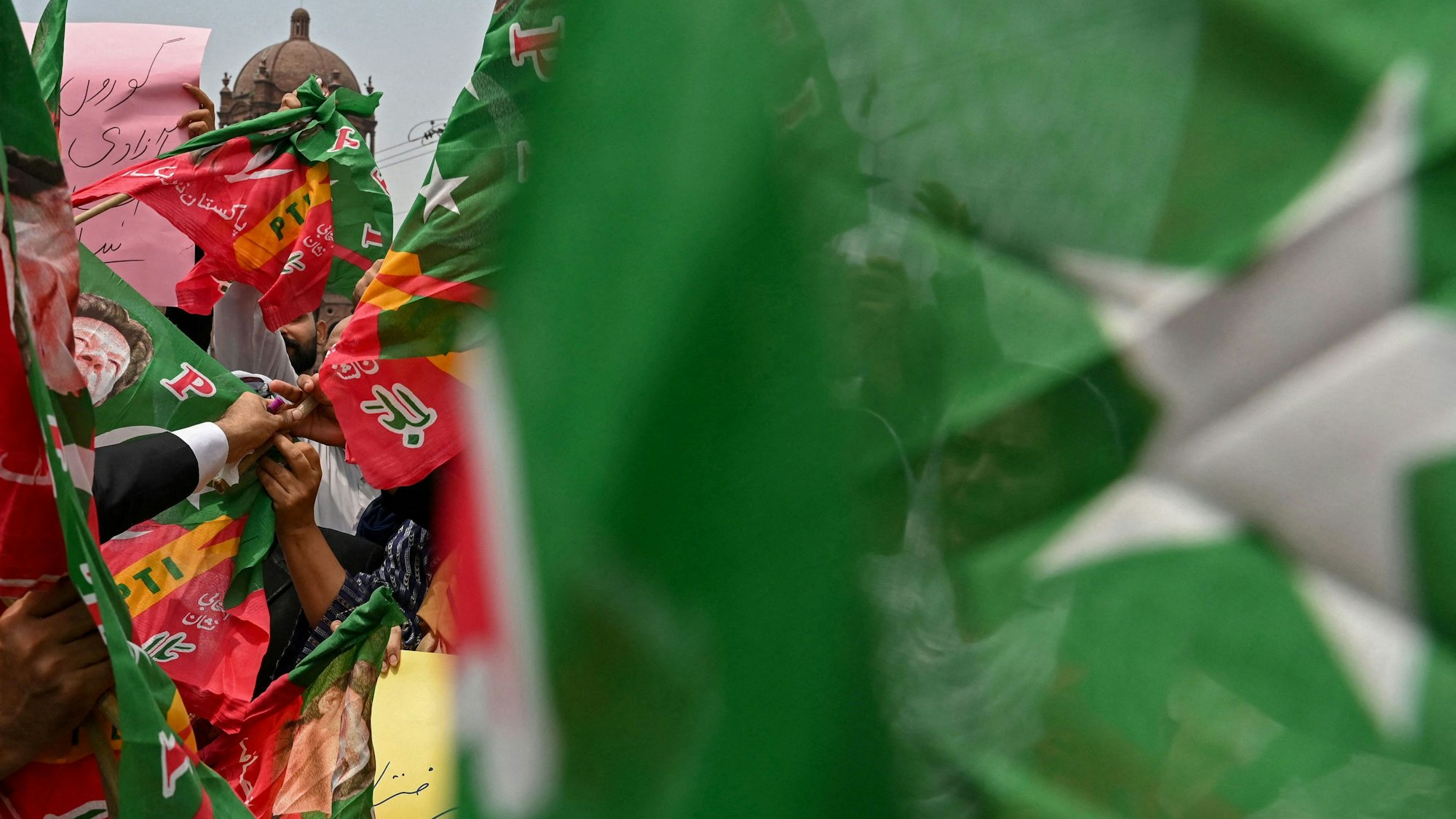 Menschen halten Banner hinter einer unscharfen pakistanischen Flagge hoch. (Symbolbild)