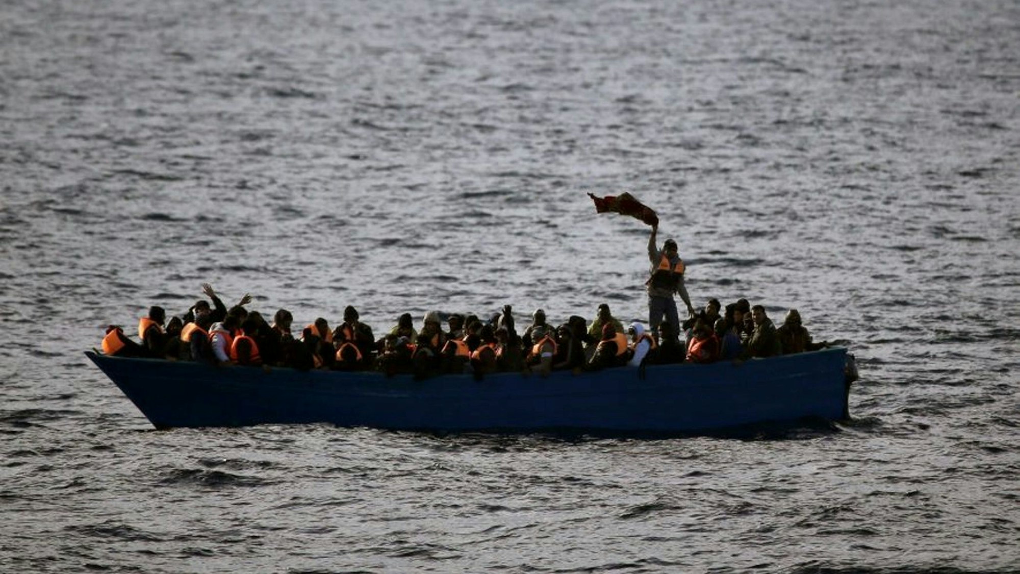 Geflüchtete aus Afrika rufen auf dem Mittelmeer in einem Boot um Hilfe.