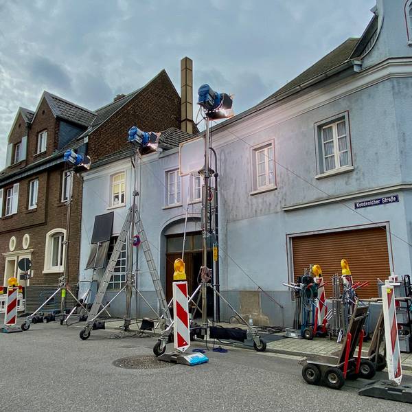 Das Bild zeigt ein Wohnhaus, an dem für die Dreharbeiten große Scheinwerfer aufgebaut und weitere Filmausrüstung abgestellt wurden.