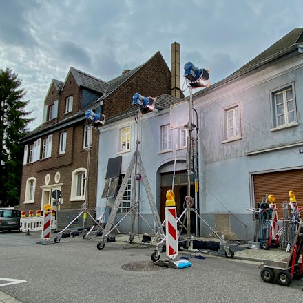 Das Bild zeigt ein Wohnhaus, an dem für die Dreharbeiten große Scheinwerfer aufgebaut und weitere Filmausrüstung abgestellt wurden.