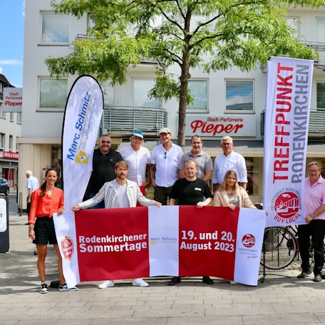Eine Gruppe von Männern und Frauen präsentiert Werbefahnen auf einem Marktplatz.