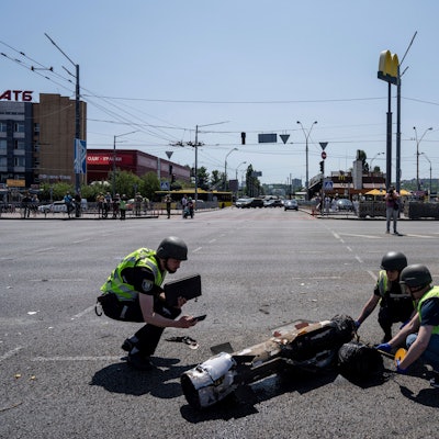 Ukrainische Polizisten knien vor einem Raketensplitter nach einem russischen Raketenangriff auf die ukrainische Hauptstadt Kiew.
