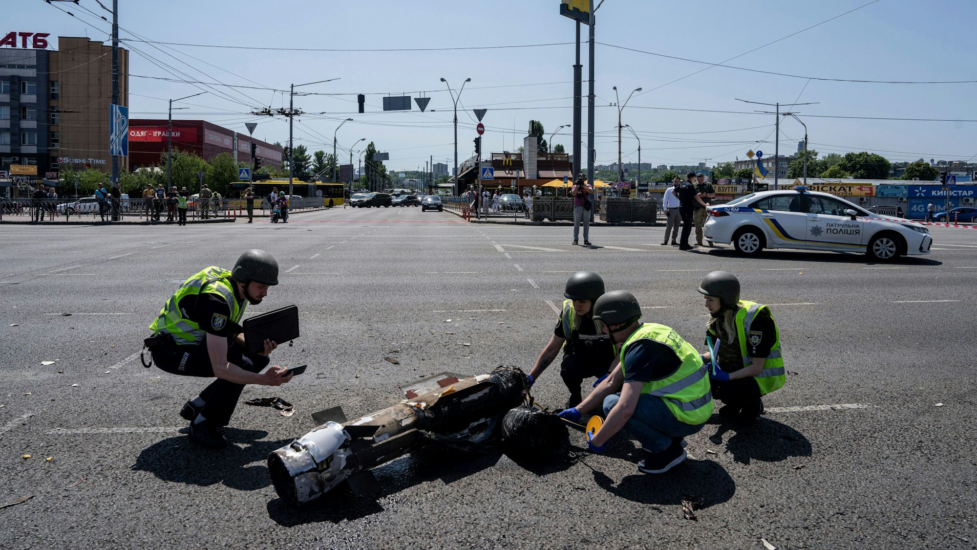 Ukrainische Polizisten knien vor einem Raketensplitter nach einem russischen Raketenangriff auf die ukrainische Hauptstadt Kiew.