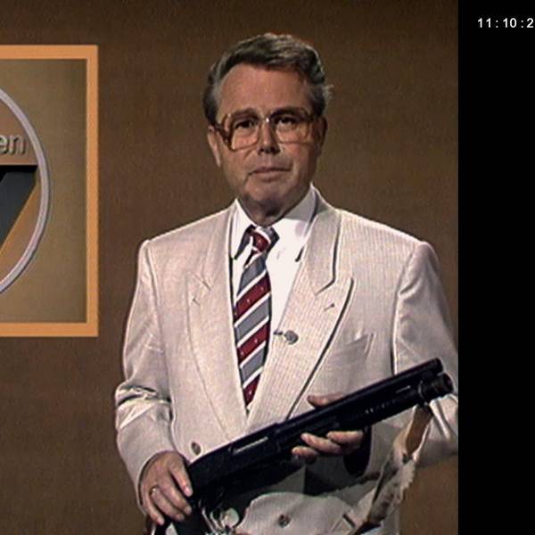 Eduard Zimmermann vor beigem Hintergrund, mit einer Waffe in der Hand im Studio von „Aktenzeichen XY ... ungelöst“.
