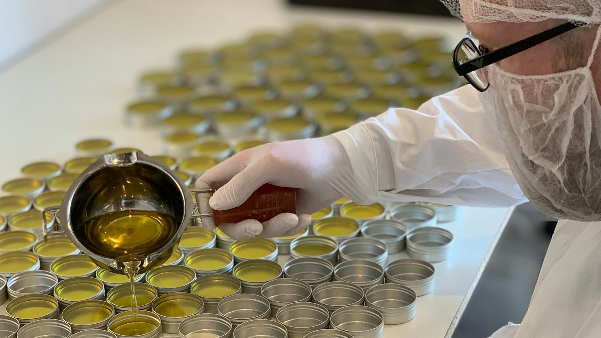 Auf dem Foto ist zu sehen, wie Marko Schulze den flüssigen Balsam in kleine Büchsen verteilt.
