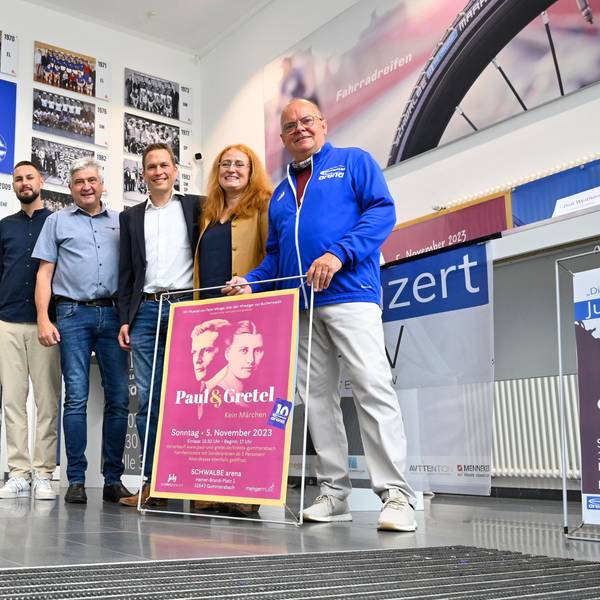 Mehrere Männer und Frauen stehen mit einem neuen Veranstaltungsprogramm in einem großen Bilderrahmen in der Halle der Schwalbe-Arena.