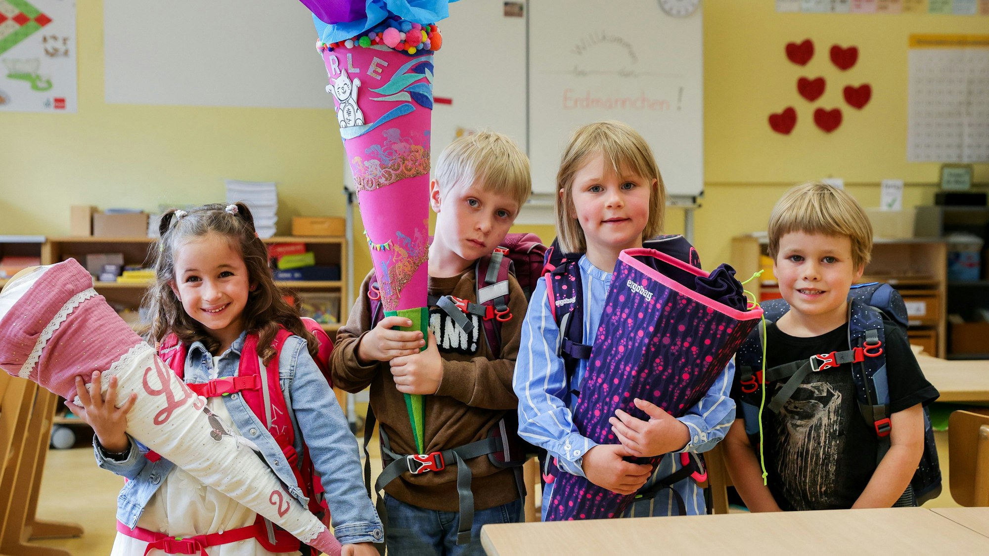 Vier Erstklässler posieren mit ihren Schultaschen und den Ranzen in ihrer Klasse.