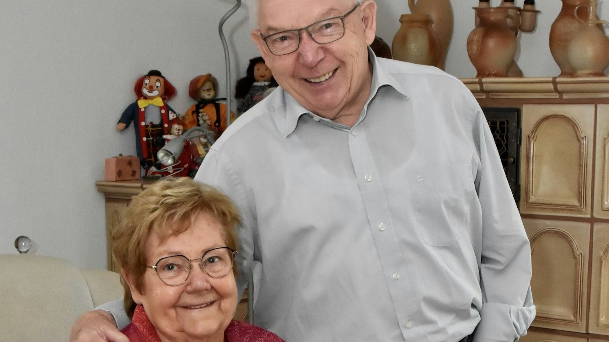 Zwei ältere Menschen lächeln in die Kamera. Der Mann legt seinen Arm und seine Frau.